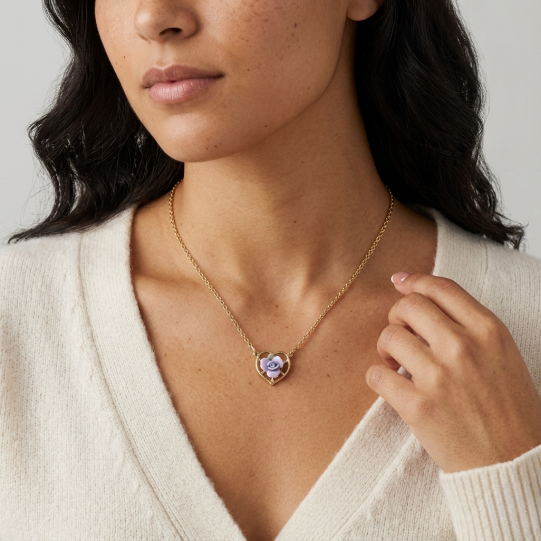 Woman wearing a gold necklace with a heart-shaped purple porcelain rose pendant against a neutral background