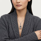 Woman wearing a gray cable knit sweater with a necklace featuring a clear glass pendant.
