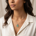 Woman wearing a necklace with an aquamarine frosted glass pendant against a neutral background
