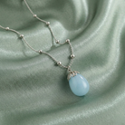 Necklace with a light blue frosted glass pendant on a green satin background