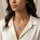 Woman wearing a necklace with a light blue frosted glass pendant against a neutral background