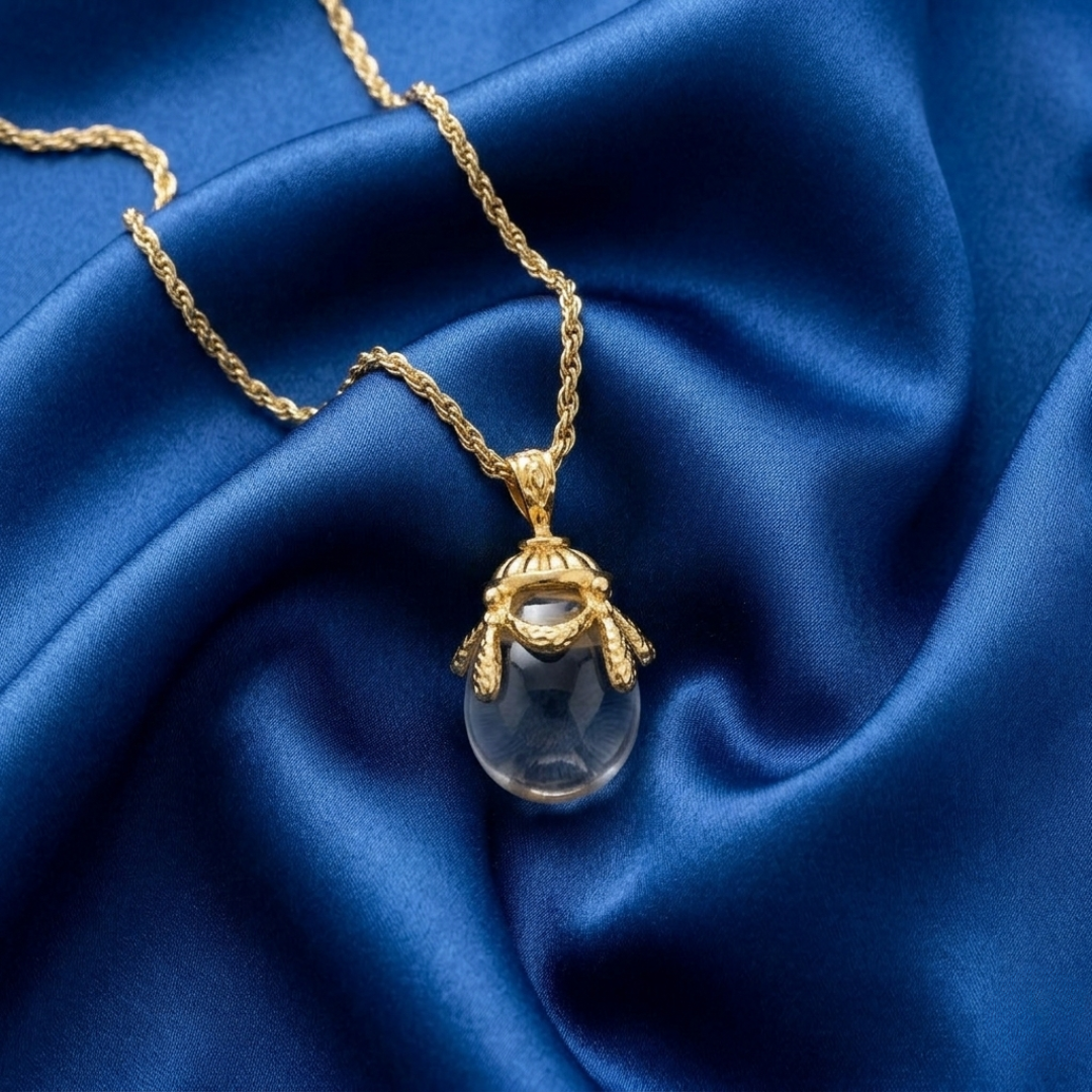 Gold necklace with a translucent egg-shaped pendant on blue fabric