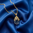 Gold necklace with a translucent egg-shaped pendant on blue fabric