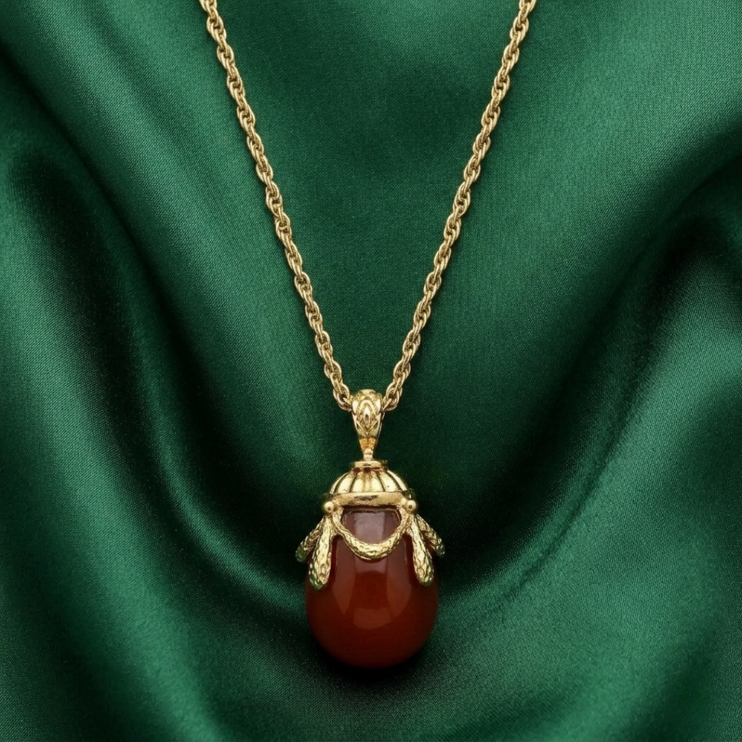 Gold necklace with a red egg pendant on a green fabric background