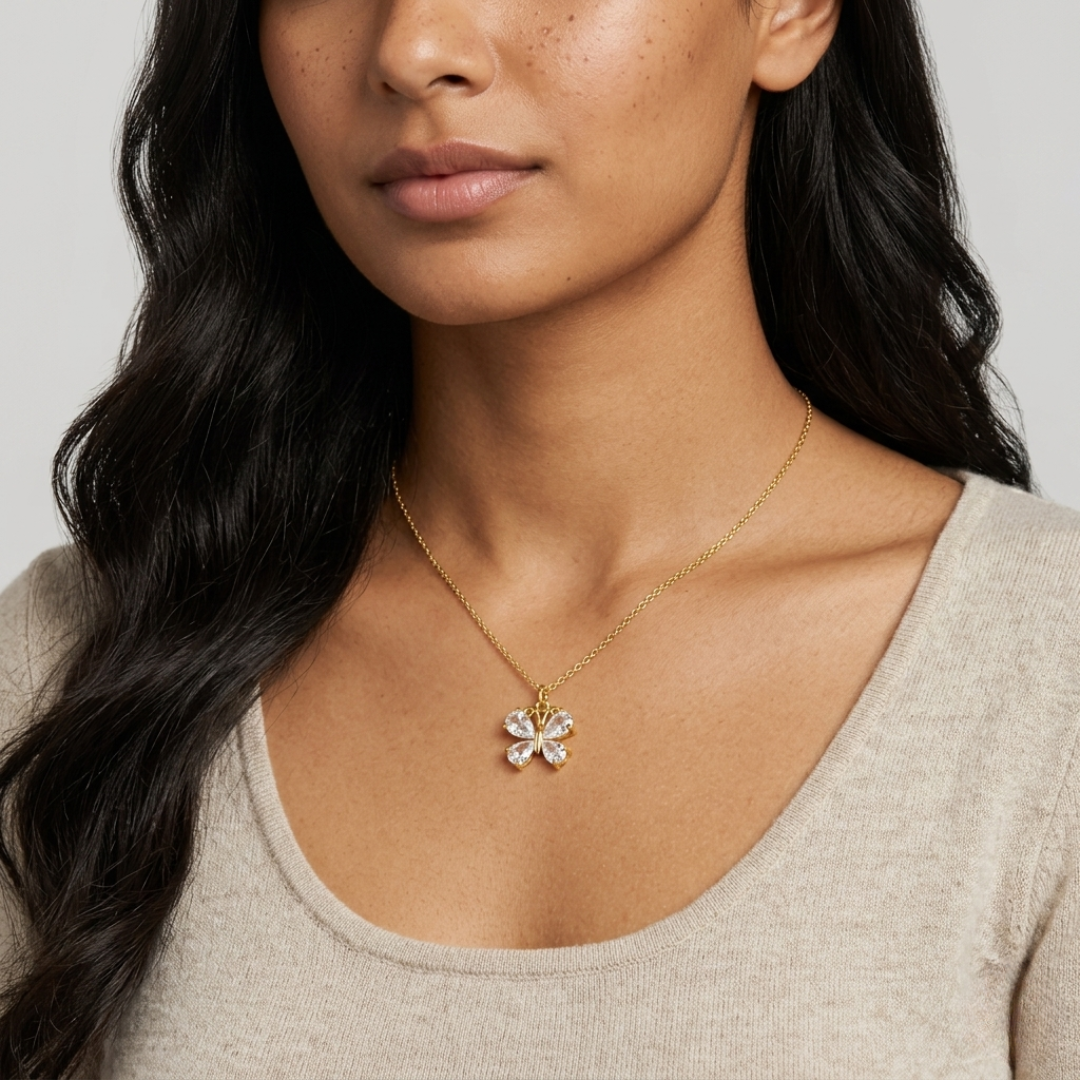 Woman wearing a gold necklace with a butterfly pendant against a neutral background