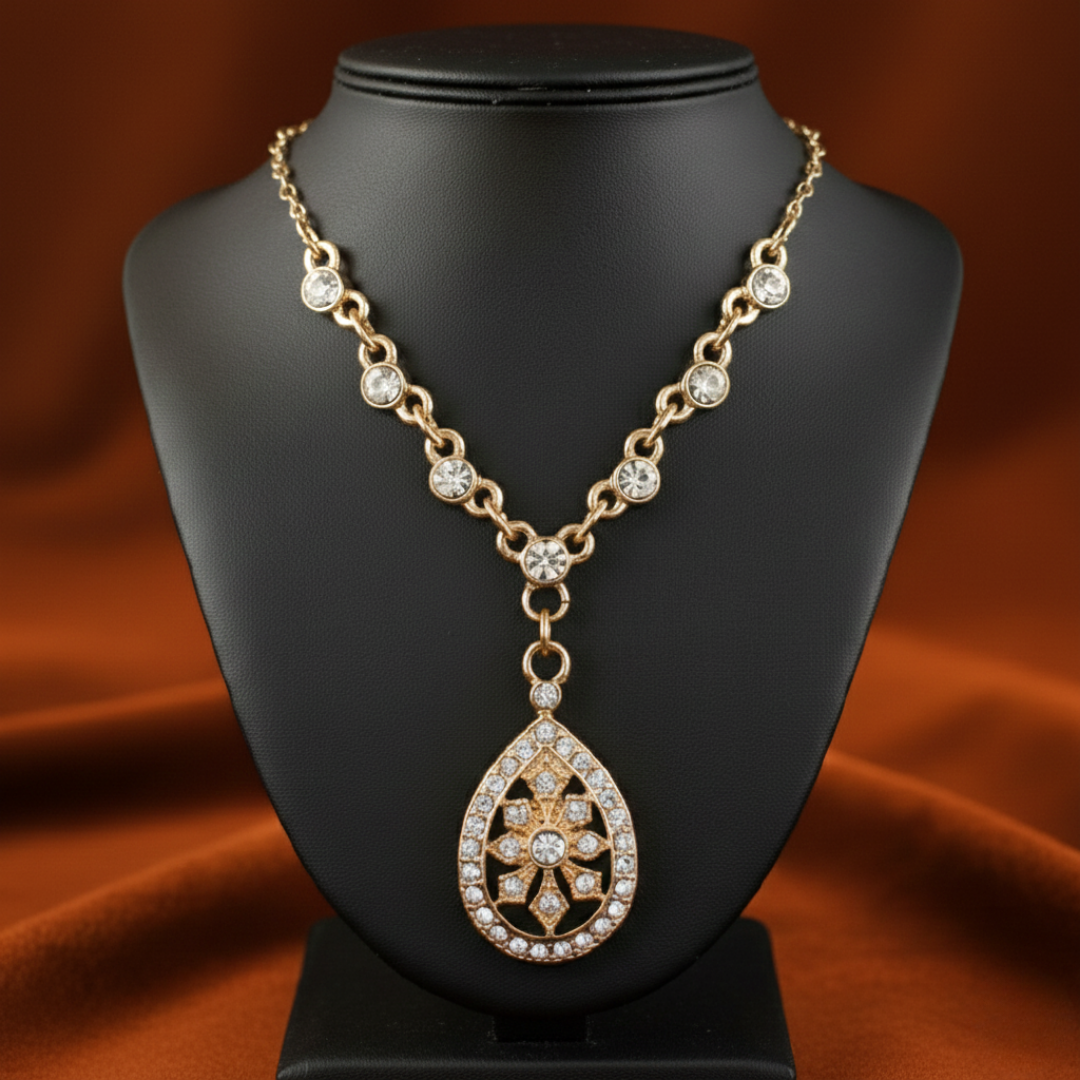 Gold necklace with a teardrop pendant on a black mannequin bust against an orange fabric background.