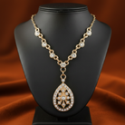 Gold necklace with a teardrop pendant on a black mannequin bust against an orange fabric background.