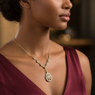 Woman wearing a gold necklace with a teardrop pendant against a blurred background.
