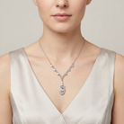 Woman wearing a silver necklace with a large crystal pendant against a neutral background