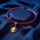 Red choker necklace with a cameo pendant on a blue fabric background