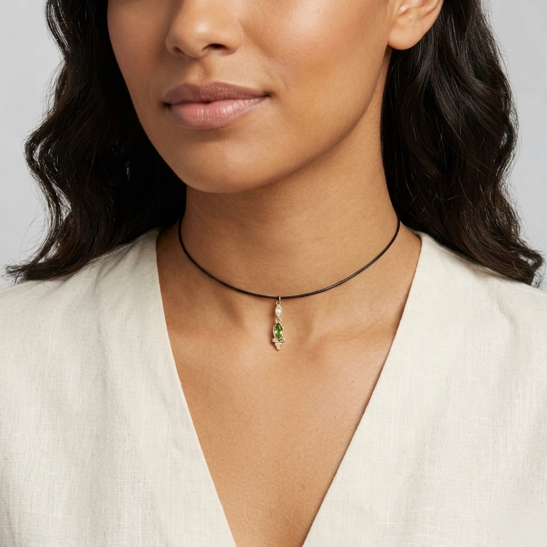 Woman wearing a choker necklace with a green crystal pendant on a plain background