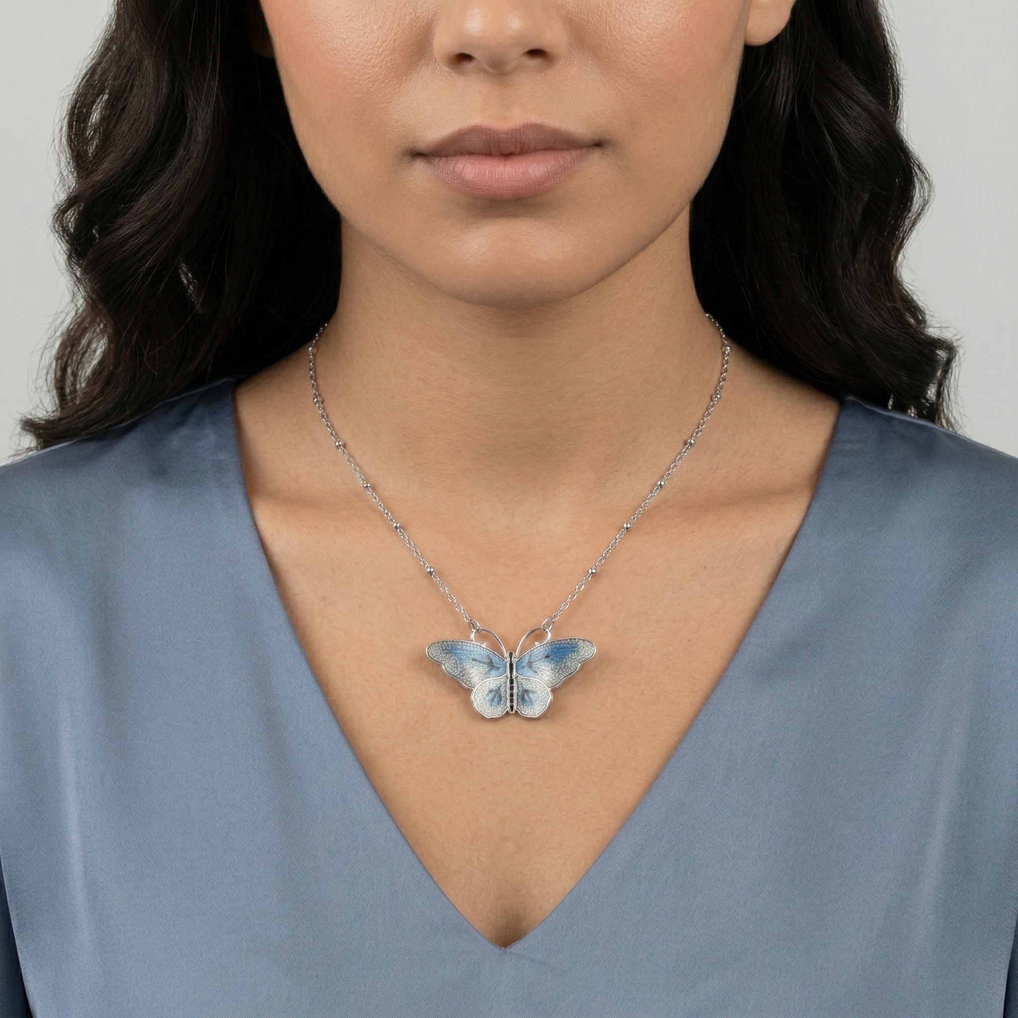 Woman wearing a butterfly necklace against a neutral background