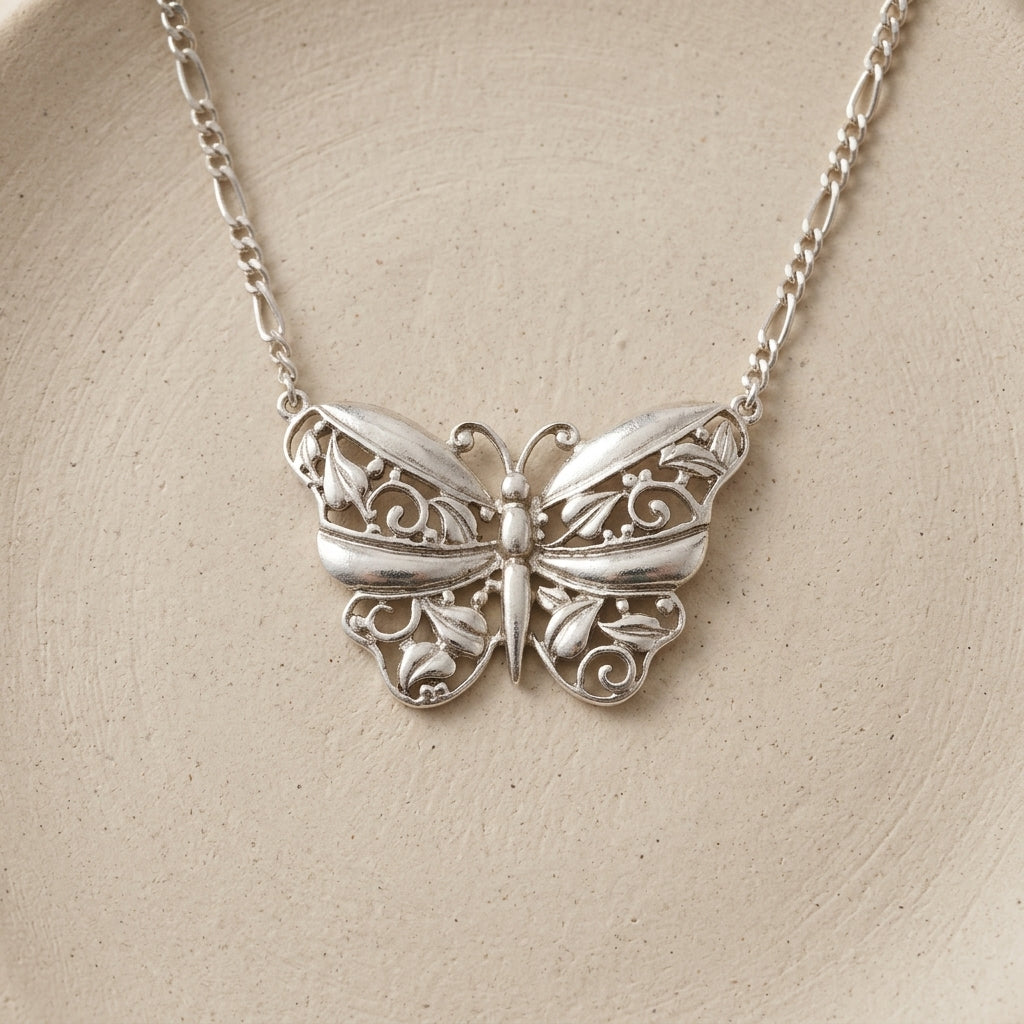 A silver butterfly pendant necklace with intricate filigree detailing, displayed on a textured beige surface.