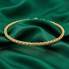 Gold braided choker necklace on a green fabric background