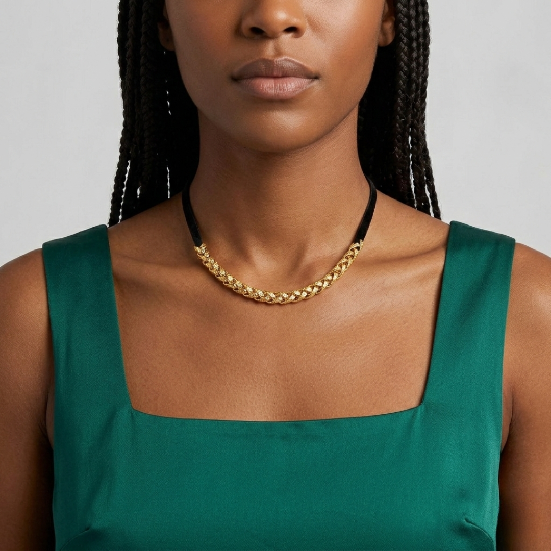 Woman wearing a gold chain choker necklace and green top against a gray background