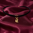 Black choker necklace with gold heart lock and key charm on a burgundy fabric background