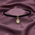 Black choker necklace with a gold and crystal pendant on a purple fabric background