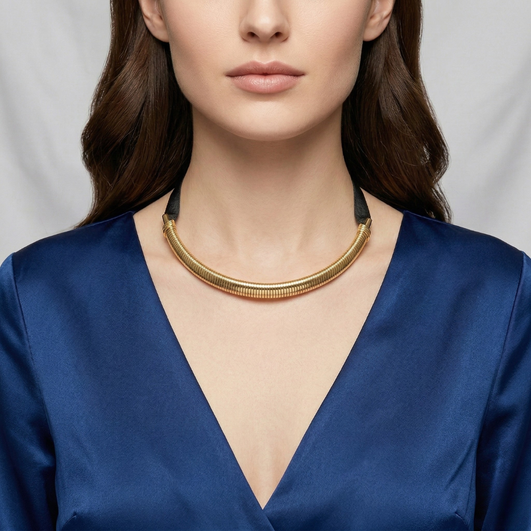 Woman wearing a gold cobra choker necklace with a blue top against a gray background