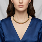Woman wearing a gold cobra choker necklace with a blue top against a gray background