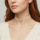 Close-up of a woman wearing a gold choker necklace with a light pink gemstone on a neutral background