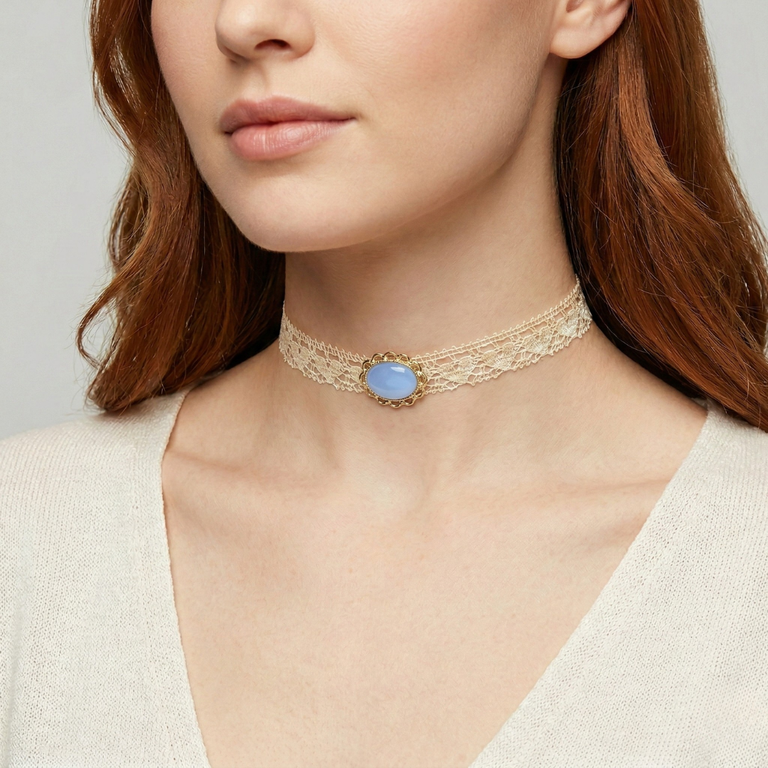 Close-up of a woman wearing a gold choker necklace with a light blue gemstone on a neutral background