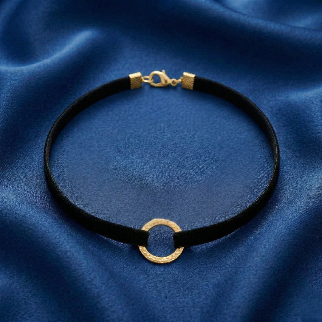 Black choker necklace with gold clasp on a blue fabric background