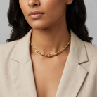 Woman wearing a gold necklace with multiple types of beads on a neutral background