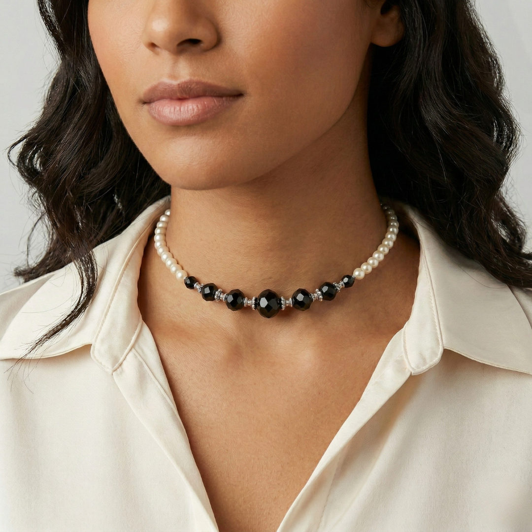 Close-up of a woman wearing a faux pearl and black bead necklace against a neutral background