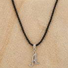 Necklace with a silver 'A' pendant on a black cord against a beige background