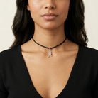 Woman in a black top wearing a black choker cord necklace with a silver tone initial pendant that has clear crystal accents