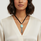 Woman wearing a necklace with a turquoise pendant on a plain background