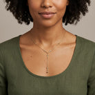 Woman wearing a gold necklace with a cross pendant on a neutral background