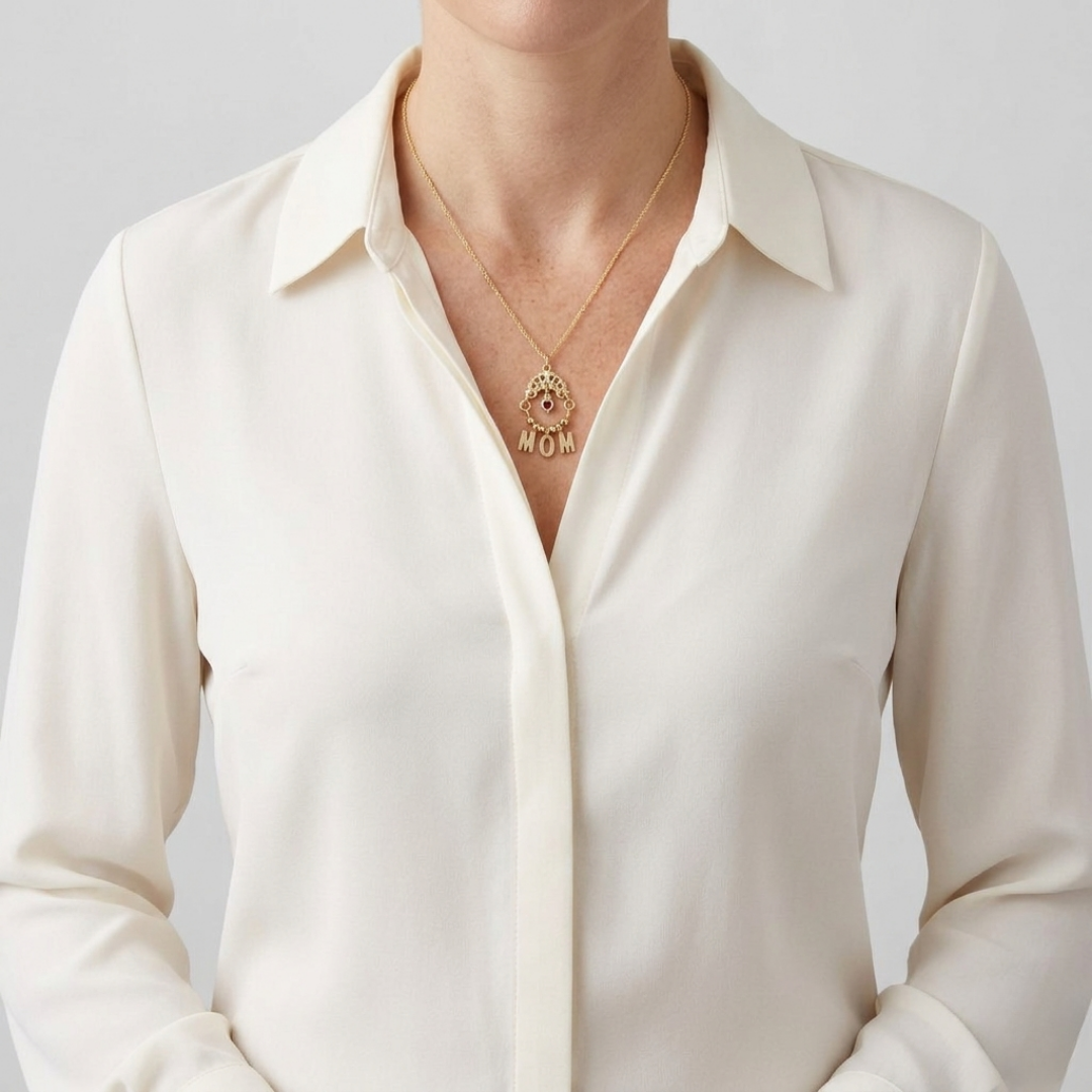 Person wearing a white shirt with a gold necklace featuring a 'MOM' pendant on a plain background