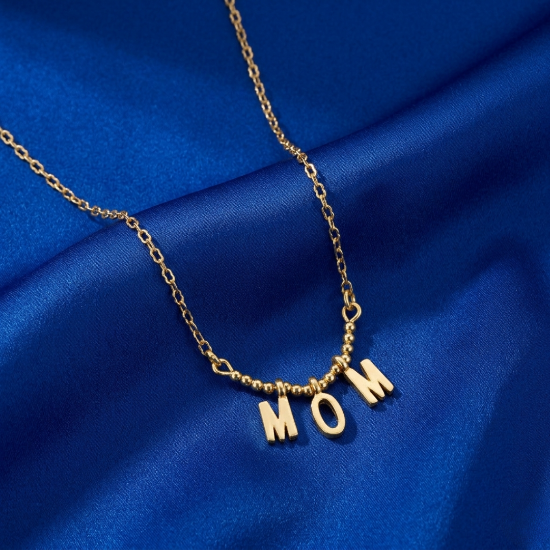 Gold necklace with 'MOM' pendant on a blue fabric background