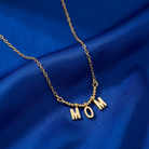 Gold necklace with 'MOM' pendant on a blue fabric background