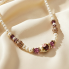 Faux pearl necklace with purple and gold beads on a beige fabric background.