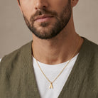 Man wearing a gold necklace with a 'A' pendant against a neutral background