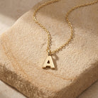 Initial Letter "A" Pendant Necklace resting on a light brown stone surface
