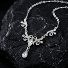 Silver tone crystal necklace with a teardrop pendant on a dark stone surface