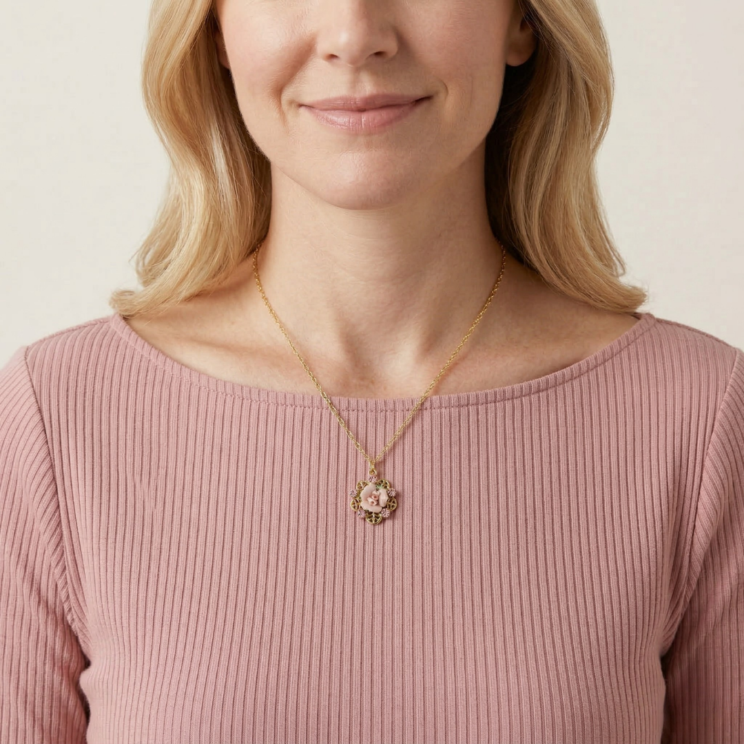 Woman wearing a gold necklace with a pink rose pendant and a pink top against a neutral background