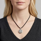 Person wearing a necklace with a circular locket pendant on a plain background