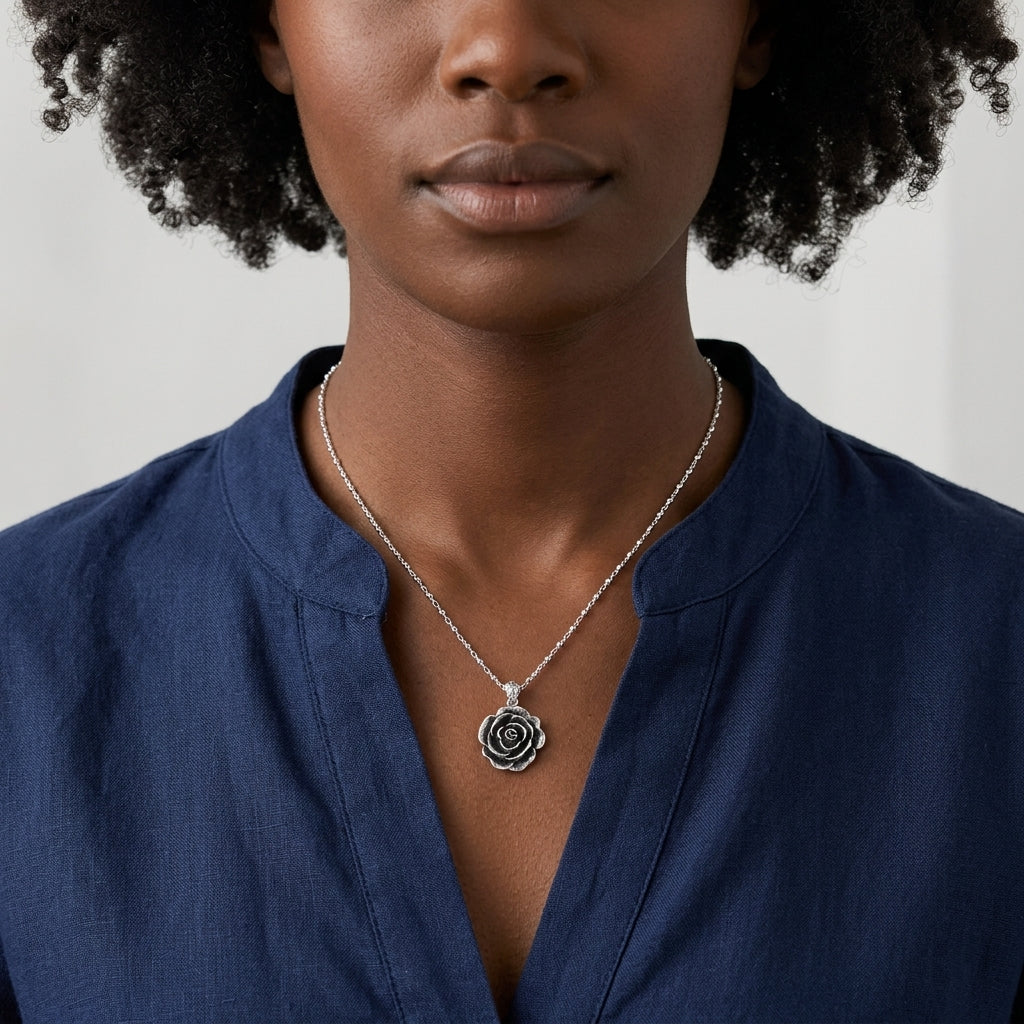 Woman wearing a silver necklace with a rose pendant against a neutral background