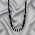 Black beaded necklace with silver accents on a gray fabric background