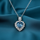 Heart-shaped necklace with blue gemstone and silver chain on a blue fabric background