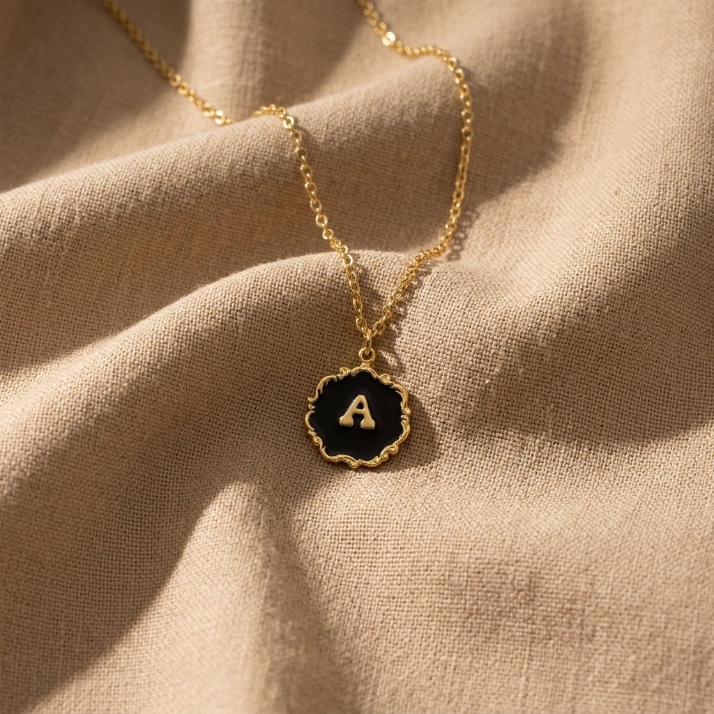 Sunburst Black Enamel Initial Pendant Necklace resting on beige linen fabric