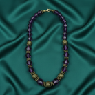 Purple beaded necklace with gold accents on a teal satin background