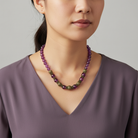 Woman wearing a purple beaded necklace against a neutral background