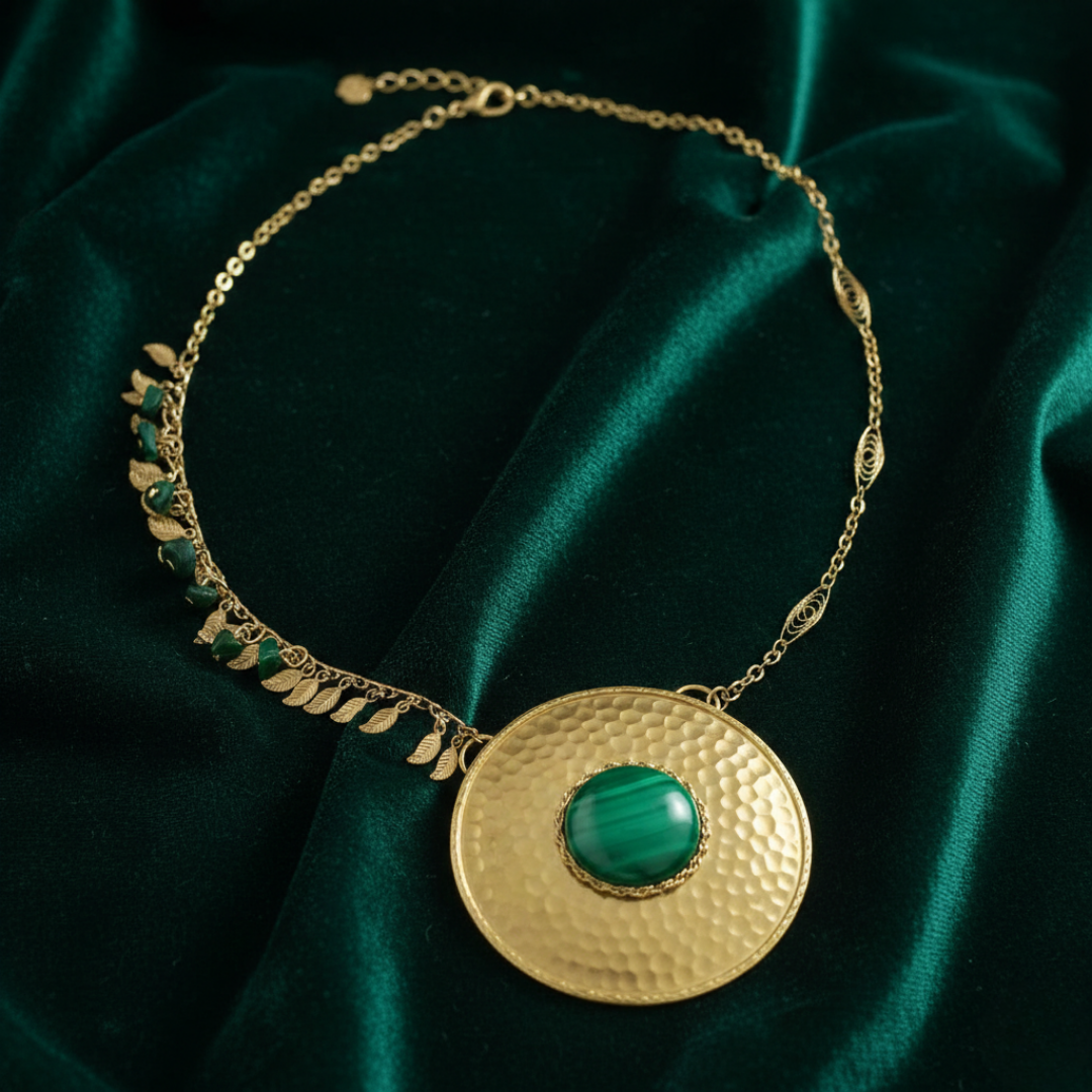 Gold necklace with a green gemstone pendant on a dark green fabric background