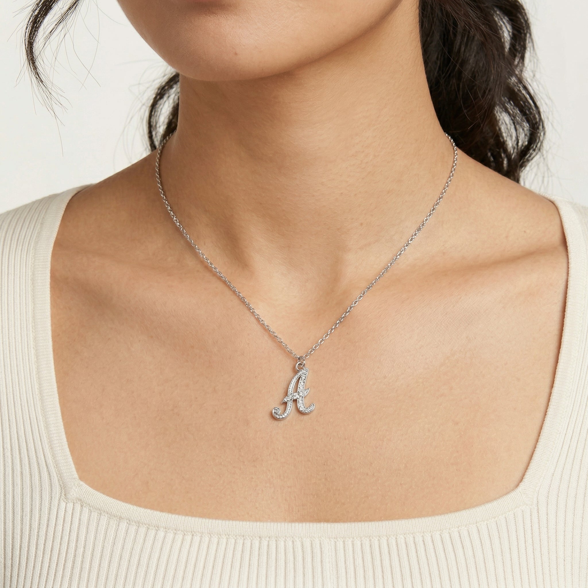 Silver necklace with a letter 'A' pendant on a person wearing a white top.