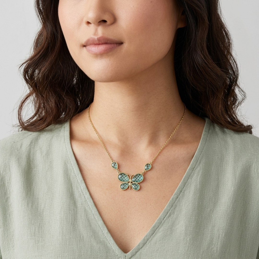 Woman wearing a gold necklace with a green butterfly pendant against a neutral background